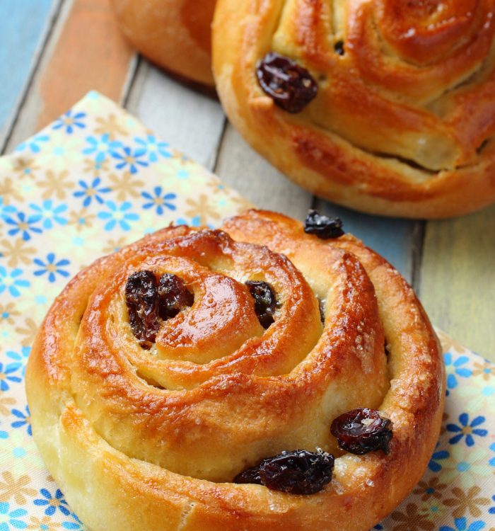 Fresh sweet swirl buns with raisins on colored wooden table